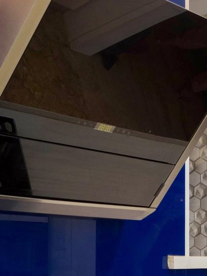 A close-up on a modern, angled chimney hood. The sleek black glass finish complements the bold blue cabinetry in this contemporary kitchen design.