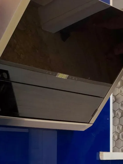 A close-up on a modern, angled chimney hood. The sleek black glass finish complements the bold blue cabinetry in this contemporary kitchen design.
