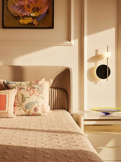 A close-up of a bedroom in one of the apartments, where soft, natural light highlights the textures of the bedding, wall molding, and a contemporary bedside lamp.