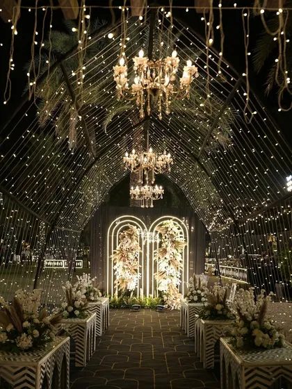 This is how I turn a sangeet night into a celestial dream. A grand tunnel entrance adorned with thousands of fairy lights and elegant chandeliers guides guests into a starry night themed celebration, promising an evening of wonder.