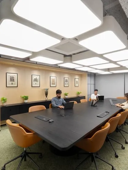 A spacious boardroom with a dark, angular table and comfortable orange chairs. The custom overhead lighting fixture follows the shape of the table, creating a cohesive design.