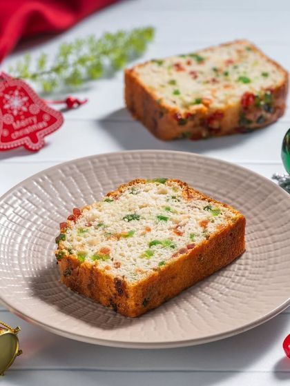A slice of light fruit cake with colorful tutti-frutti, shot in a bright, high-key style for a Christmas catalog.
