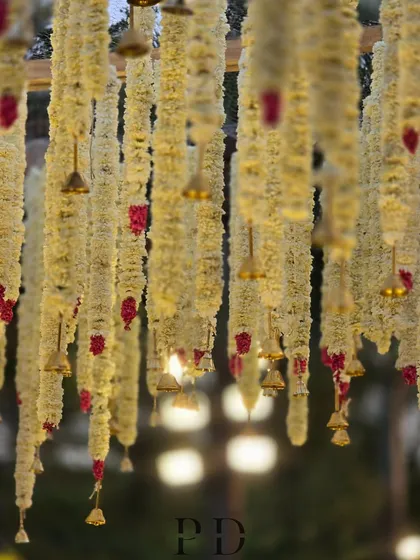 A view from underneath the floral canopy of a mandap, showing the hanging tuberose garlands and small brass bells.