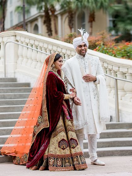 A classic portrait on the steps. The bride's rich, multi-toned heritage lehenga with a double dupatta contrasts beautifully with the groom's elegant ivory sherwani.