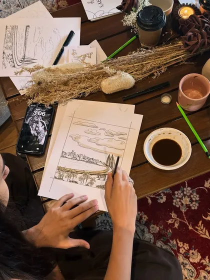 A participant at a private event working on their sketch of the Mumbai sea link, with beautiful table decor setting the mood.
