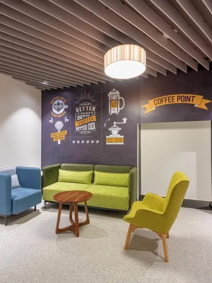 A coffee and collaboration lounge with comfortable seating and a feature wall with coffee-themed typography. A decorative wooden screen provides partial separation from the main office.
