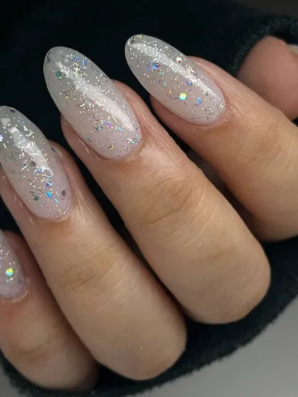 A beautiful, iridescent glitter manicure on long, almond-shaped nails. The multi-colored glitter particles create a magical, unicorn-like effect.