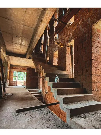 The interior of a home during construction, showing the raw beauty of the laterite brick and exposed concrete staircase. This stage reveals the skeleton of the building before finishing materials are applied.
