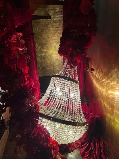 A close-up look at how we combine different elements to create a dramatic mood. A magnificent crystal chandelier is intertwined with deep crimson florals and rich velvet, adding layers of texture and luxury to the decor.