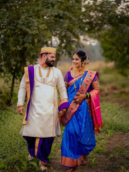 A lovely shot of a Maharashtrian couple walking together through a green, natural path, holding hands and sharing a smile.