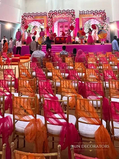 The guest seating is part of the decor. Here, chairs are adorned with bright orange and pink drapes, complementing the stage and ensuring the entire venue is bursting with color.