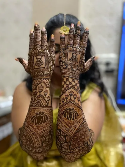 A bride showing off her full-arm mehandi, which features large lotus motifs and traditional symbols like the kalash.