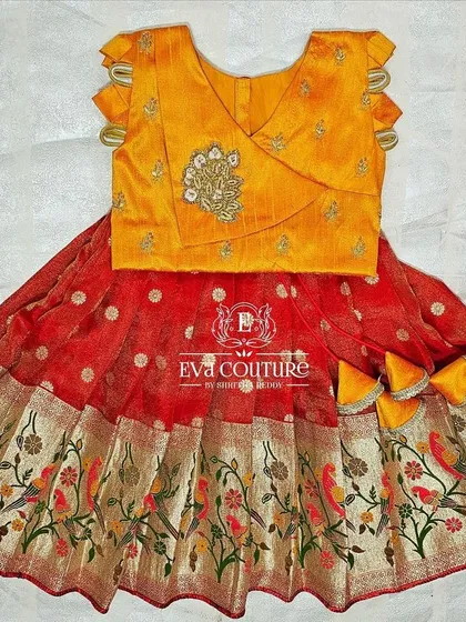 A newborn-sized lehenga with a Paithani-style bird print border. The yellow blouse has a modern wrap-style design.