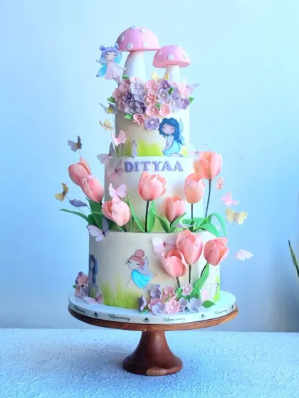 A stunning three-tier enchanted forest cake with tulips, fairies, and toadstools. This cake is designed with moving butterfly wings for an extra magical effect.