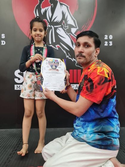 A young girl smiles with her medal and certificate. Competing helps build confidence and sportsmanship in our little warriors.