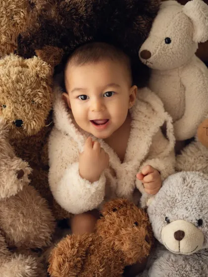 A baby smiles from a sea of cuddly teddy bears. This is a super cute and cozy idea for a baby photoshoot.