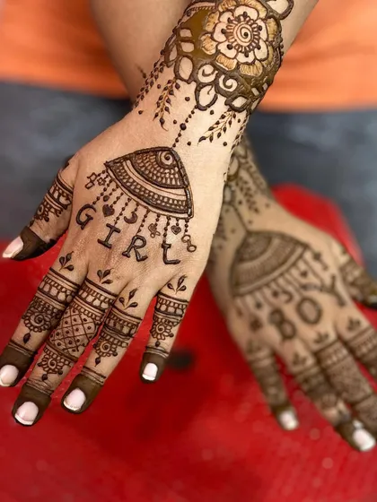A simple yet beautiful baby shower design, with the word 'GIRL' written under a jhumka motif, paired with an elegant floral design on the wrist.