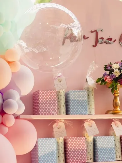 A close-up of the gift and favor display for a pastel-themed party. The setup includes a balloon garland and neatly arranged gift boxes on a shelf.