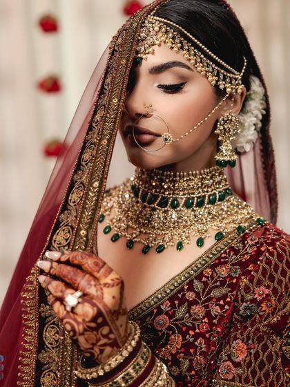A detailed shot of the bride's jewelry and makeup. The large nose ring, statement necklace, and perfectly winged eyeliner complete her classic bridal look.