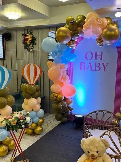 A grand 'Oh Baby' stage setup for a baby shower in a banquet hall, featuring hot air balloon props and teddy bears.