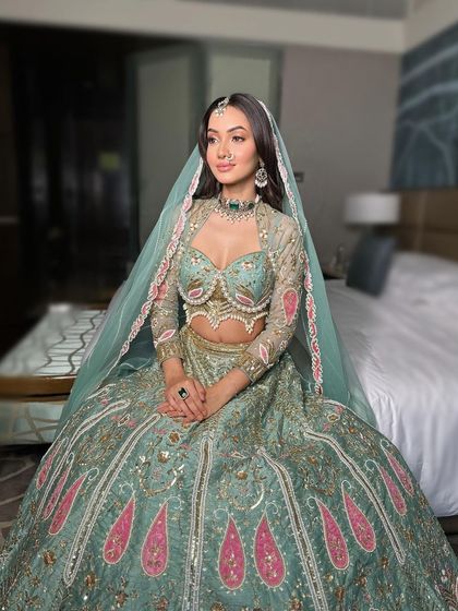 A breathtaking bridal portrait. The hair is styled in soft, open waves, tucked behind one ear to showcase the earrings, while the other side frames the face. A delicate maang tikka and sheer dupatta complete this modern bridal look.