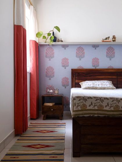 The guest bedroom, featuring a whimsical floral wallpaper and two-tone curtains. A ledge above the wallpaper offers a spot to showcase miniature brass decor pieces.