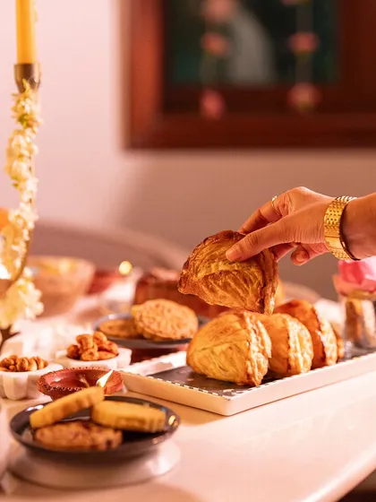 A festive table glowing with diyas, featuring our flaky puff pastry gujiyas. Our Diwali collection combines traditional flavors with contemporary forms.