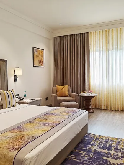 A guest room at Vivanta Bengaluru, designed as a visual retreat. The combination of a vertically-striped headboard, warm lighting, and a colorful bed runner creates a space that is both stylish and comforting.