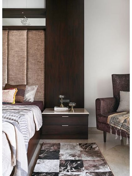 This view highlights the complete bedroom composition, from the plush upholstered headboard and dark wood paneling to the cozy armchair in the corner. A patterned rug adds texture and defines the sleeping area.
