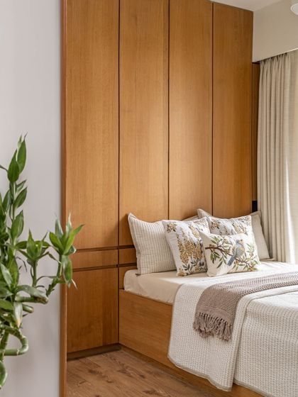The guest room is a cozy retreat with a comfortable bed set against a warm wood-paneled wall. Bright natural light and a pop of green from a plant make this room both stylish and functional.