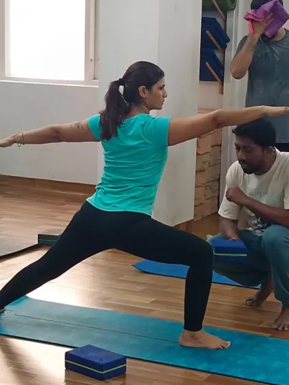 A teacher provides a subtle adjustment in Virabhadrasana II (Warrior II), helping the student find the correct alignment and energy in the pose.