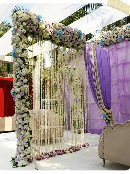 An intimate Nikah seating area, beautifully decorated with lavender drapes and an arch of white and blue flowers. The strings of jasmine flowers add a traditional and fragrant element.
