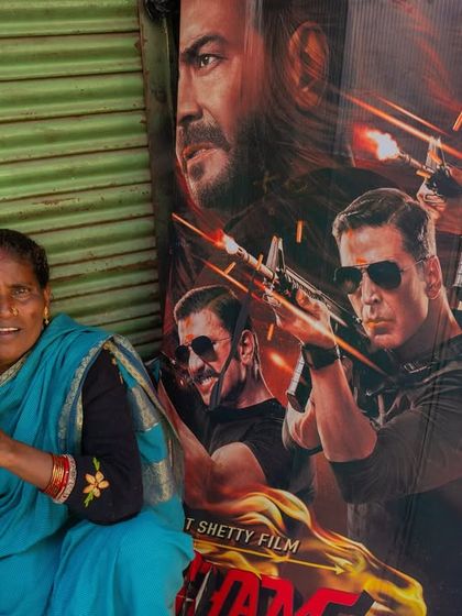 A woman sits on the street next to a large Bollywood movie poster in Kolkata. This image captures the interesting contrast between everyday life and the world of cinema.