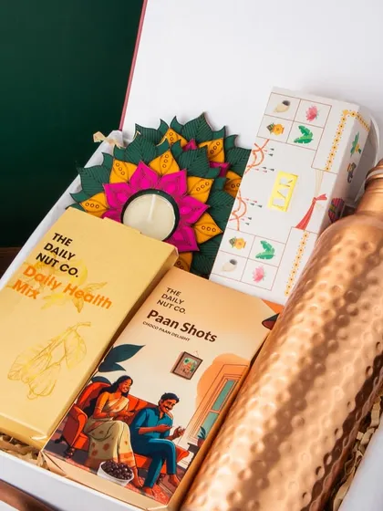 This hamper is a celebration of modern wellness and Indian tradition. It features a hammered copper bottle for health benefits, alongside The Daily Nut Co.'s health mix and paan shots, plus a beautiful diya for the festive touch.