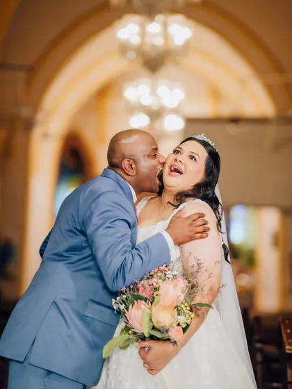 A joyful and candid moment between the bride and a family member, likely her father, sharing a laugh and a kiss on the cheek in the church.
