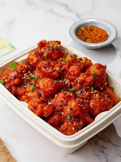 Crispy bang bang cauliflower in a takeaway container, shot on a clean marble background.