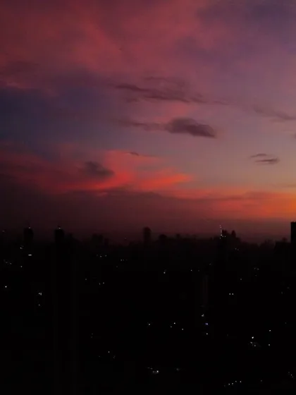 The silhouette of the Mumbai skyline is set against a dark, moody sky with streaks of orange and purple clouds after sunset.