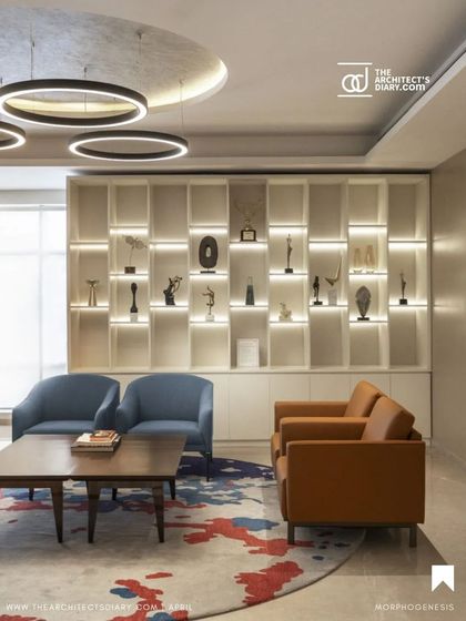 An illuminated display wall in the Adani Realty office showcases the company's achievements. The combination of warm wood tones, comfortable seating, and a vibrant rug creates a sophisticated and inviting lounge area.