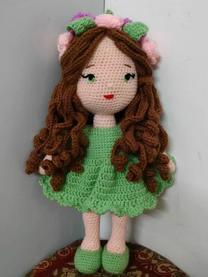 A beautiful doll with long, curly brown hair, a green dress, and a crown of pink and green flowers.