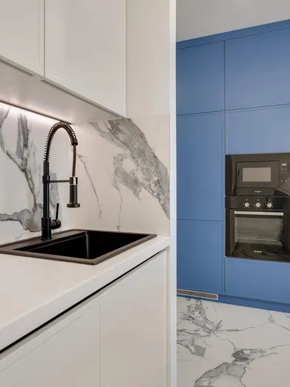 A two-tone kitchen design with bold blue cabinetry for storage and a contrasting white section for the sink area, tied together with a stunning marble floor.