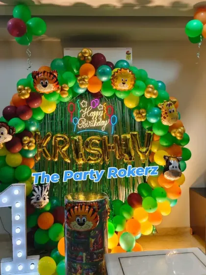 The complete jungle theme setup in a living room, including the balloon ring, a themed pedestal for the cake, and a large light-up number '1'.