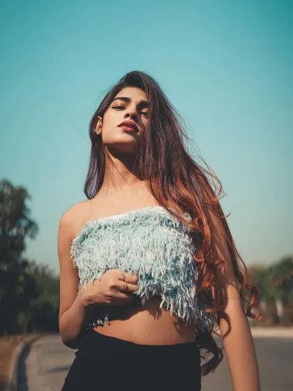 A strong, fashion-forward pose against the bright blue sky. The wind in her hair adds a sense of natural movement.