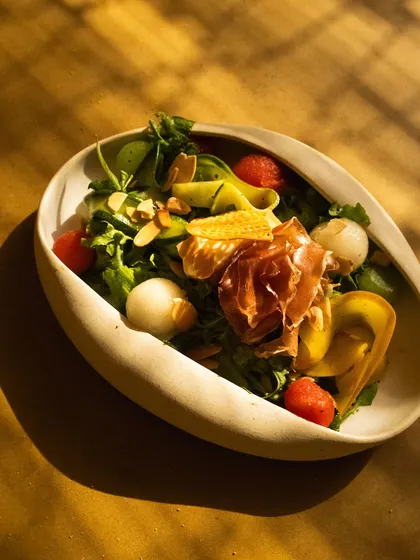 A fresh and colorful salad with prosciutto and melon, catching the beautiful striped sunlight.
