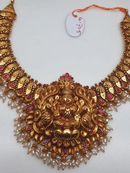This grand temple necklace features a large pendant with Goddess Lakshmi flanked by elephants. The necklace is made from 92.5 silver with gold plating and is adorned with pearls and pink stones.