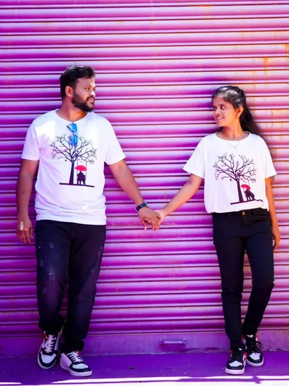 A cute pre-wedding photo with the couple in matching graphic tees, holding hands against a bright purple background.