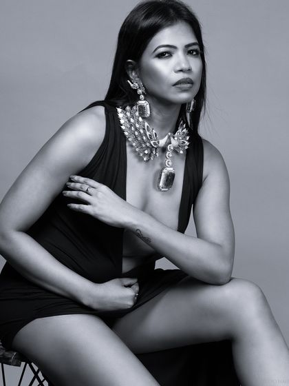 A dramatic black and white portrait of a model in a plunging black dress, adorned with a statement necklace. The lighting is moody and cinematic.
