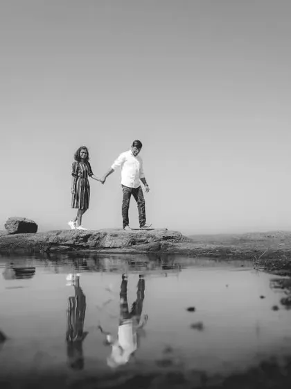 A striking black and white shot of a couple on a rock by the water, their figures perfectly reflected in the still surface. This image uses symmetry and monochrome to create a serene and artistic portrait.