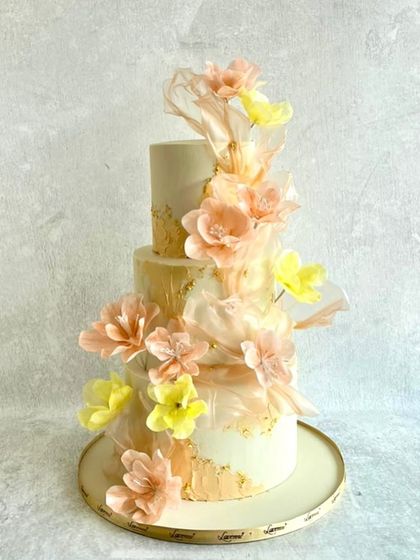 Soft, dreamy, and romantic. This engagement cake is decorated with delicate, translucent wafer paper flowers in shades of peach and yellow. The gold leaf accents add a touch of warmth and elegance.