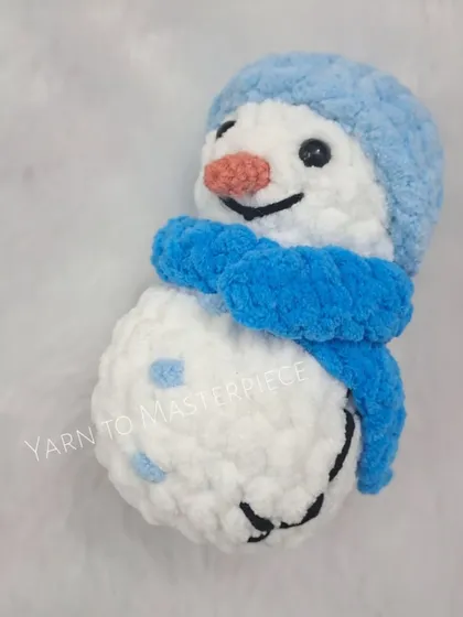 A close-up of a snowman with a light blue hat and scarf. Each one has a unique, handmade charm.