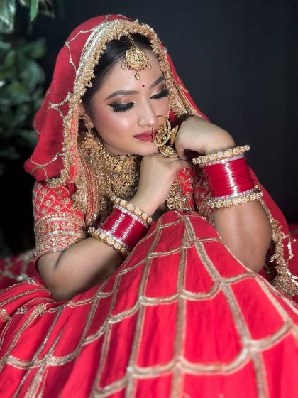 A candid moment captured. The bride is looking down, showcasing her beautiful glittery eye makeup and the rich red of her bridal lehenga.